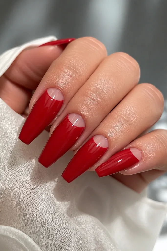 Red glossy coffin nails with a curved clear half-moon near the cuticle; the rest of the nail is solid red and the half-moon is crisp.