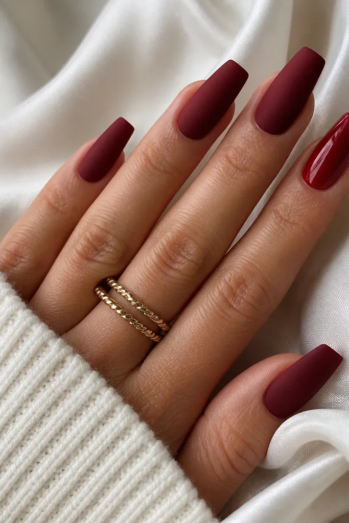 Most coffin nails are matte deep red; one nail on the ring finger is glossy red with a smooth shine.