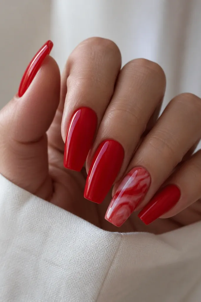All red glossy coffin nails are solid except one nail with a subtle marble swirl in lighter red and nude tones.
