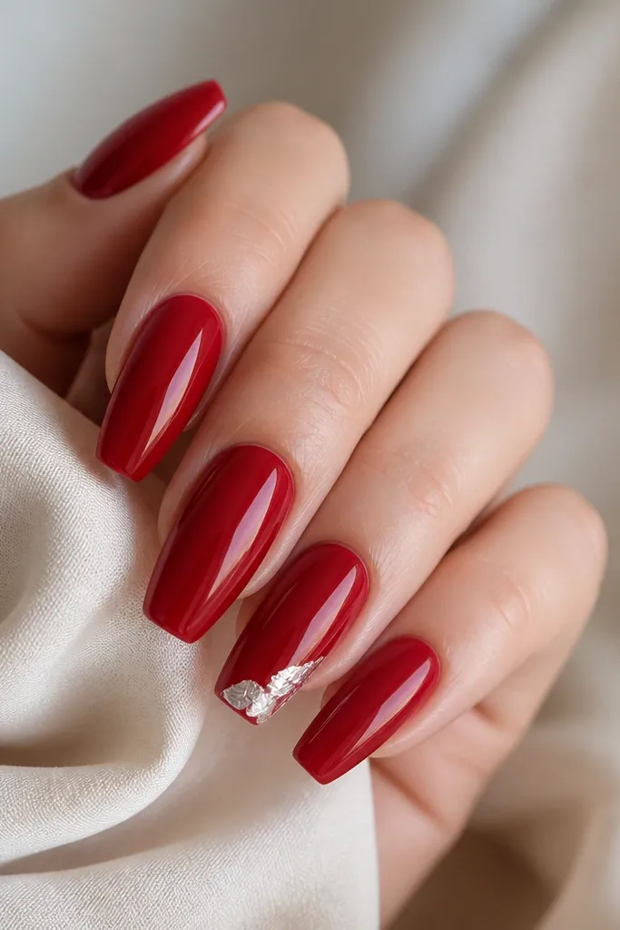 Glossy red coffin nails with a small foil fragment along the tip edge on one nail, like a metallic peel.