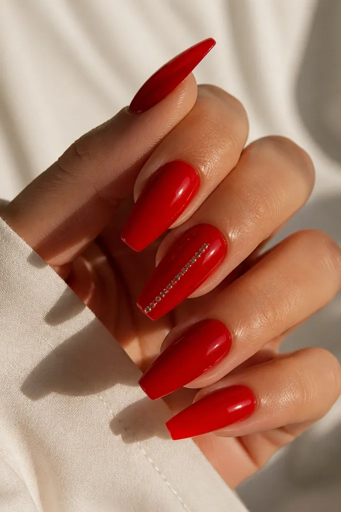Glossy red coffin nails with a single column of tiny silver dots running from mid-nail to near the tip on one accent nail.