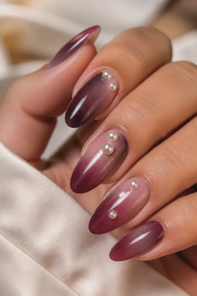 Coffin nails with a smoky plum gradient from lighter at the cuticle area to darker at the tip. On the ring finger, there are tiny pearl beads clustered in a small vertical line near the side.