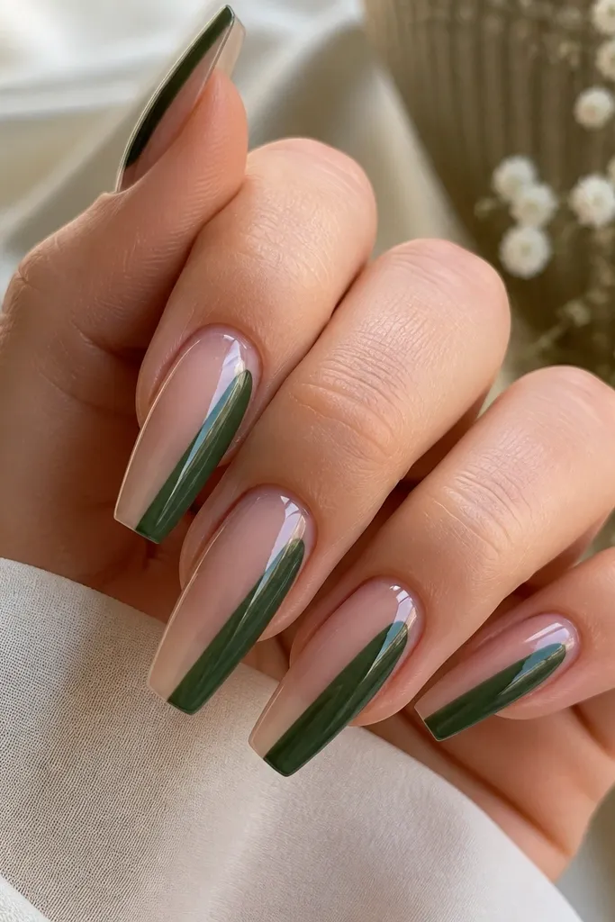 Coffin nails with a sheer nude base and glossy finish. On each nail, a bold emerald green panel sits on one side from mid-nail to tip, leaving the other side clear and nude.