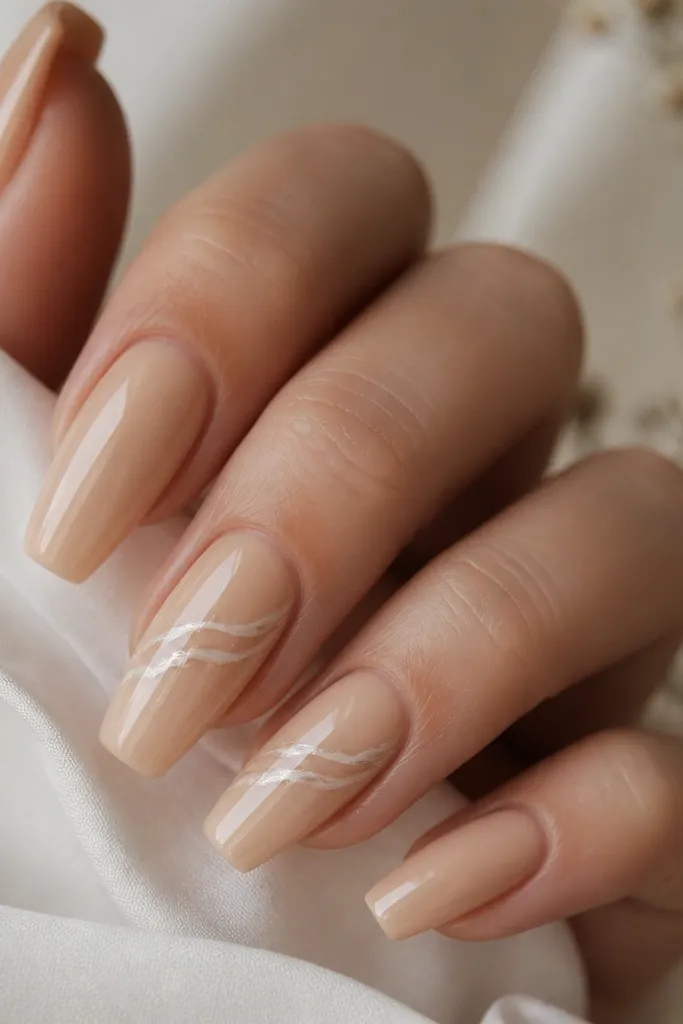 Coffin nails in champagne nude with a glossy finish. On two nails, there's a pearly swirl across the center that looks like a thin ribbon, with tiny white highlights.