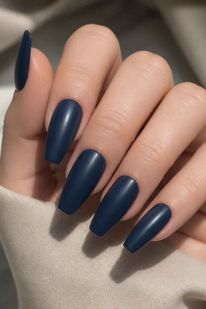 Coffin nails painted deep navy with a satin-matte finish, not flat powder matte. The nails look smooth with a soft sheen, and there's no nail art.