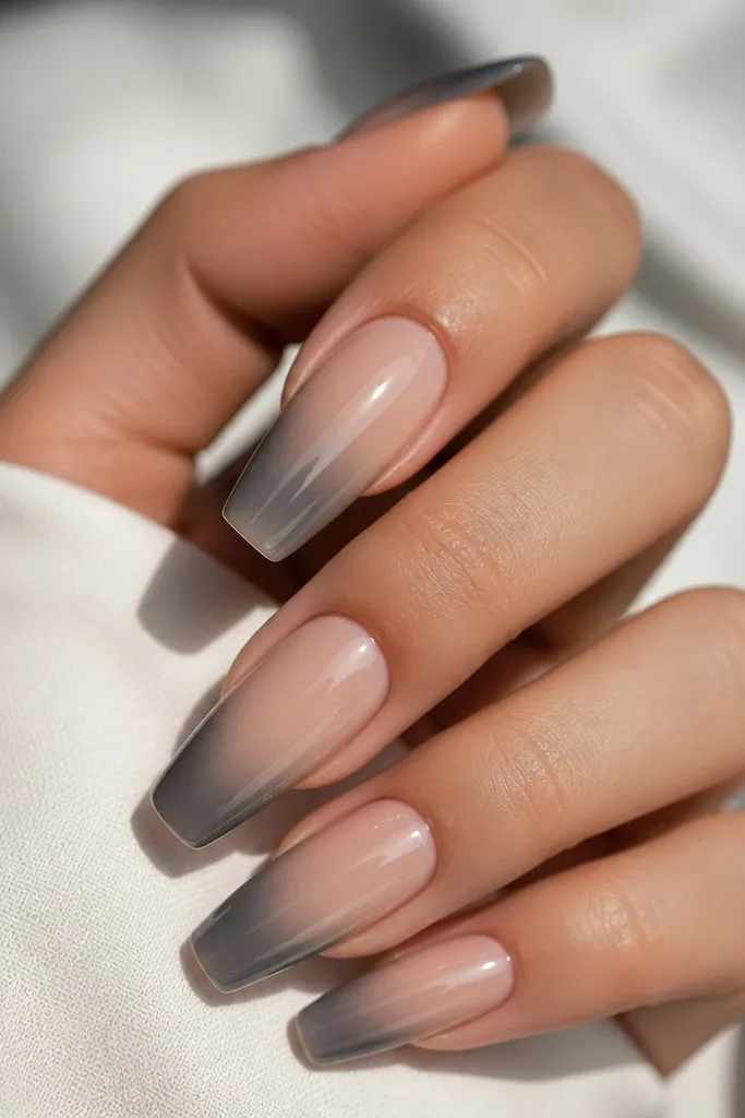 Coffin nails with a pearl nude base and glossy finish. On each nail, a smoky grey ombré sits on one side, fading from mid-nail to the tip. The other side stays mostly nude.