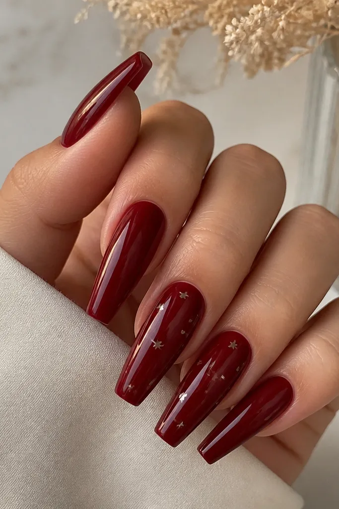 Deep cherry red coffin nails with scattered tiny silver stars across two or three nails. The stars are minimal, each about the size of a pinhead. Everything is glossy.