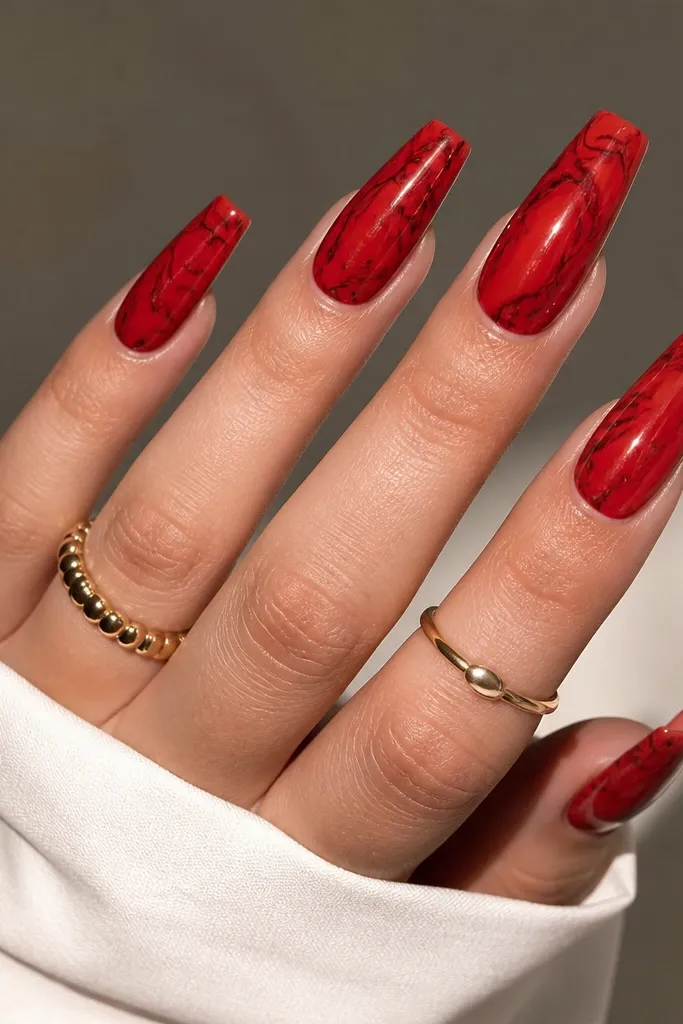 True red coffin nails with marble swirls. The swirls include thin black lines and a few darker red streaks, giving a stone-like pattern. The overall finish is glossy.