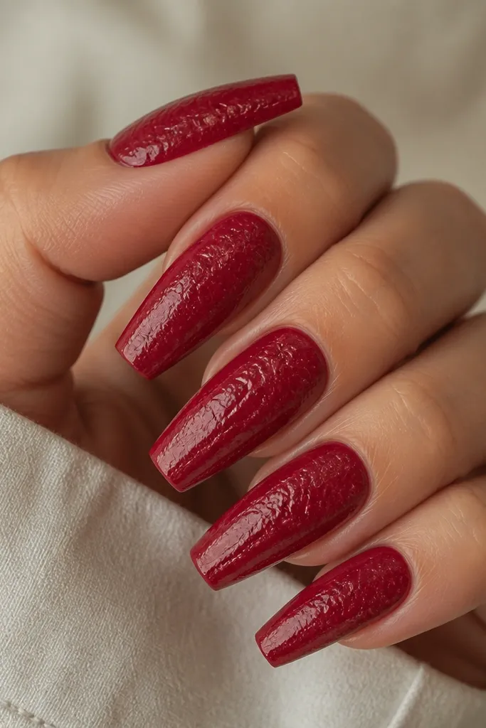 Cherry red coffin nails with a crinkled, leather-like texture. The finish has tiny ripples and a semi-gloss sheen, not smooth. No other decorations.