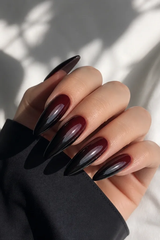 Long stiletto nails with a glossy black cherry base fading into near-black at the tips. The chrome is a smoky black that reflects like a dark mirror, with a smooth fade and clean cuticles.