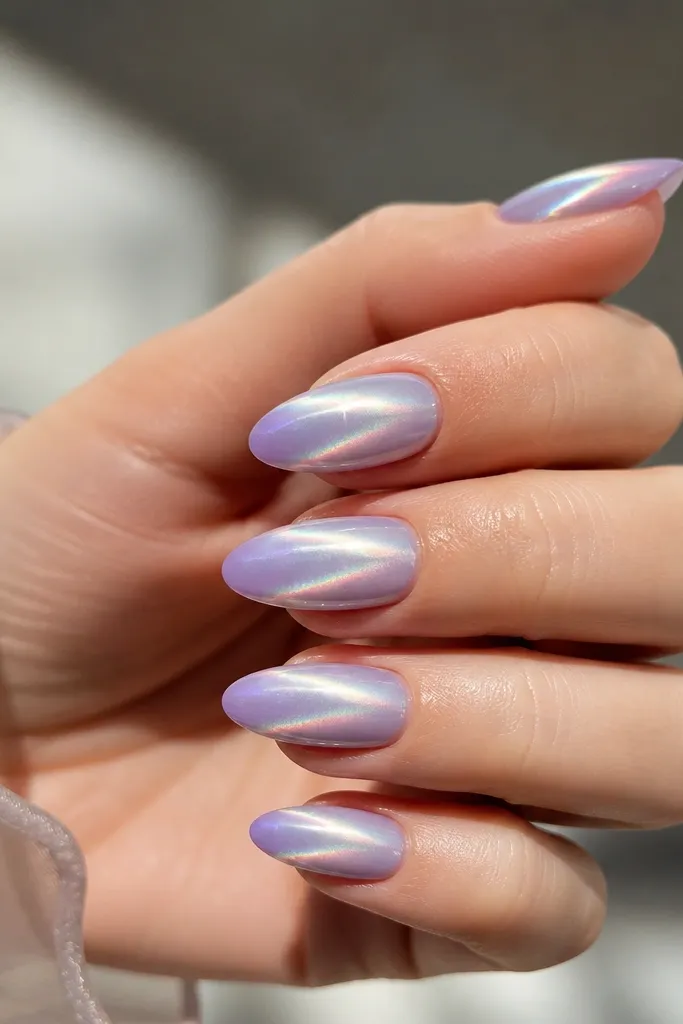 Short almond nails fading from light grey-lilac to lilac at the tip. Aurora-style chrome creates multicolor flashes, and a flare streak of light sits near the tip.