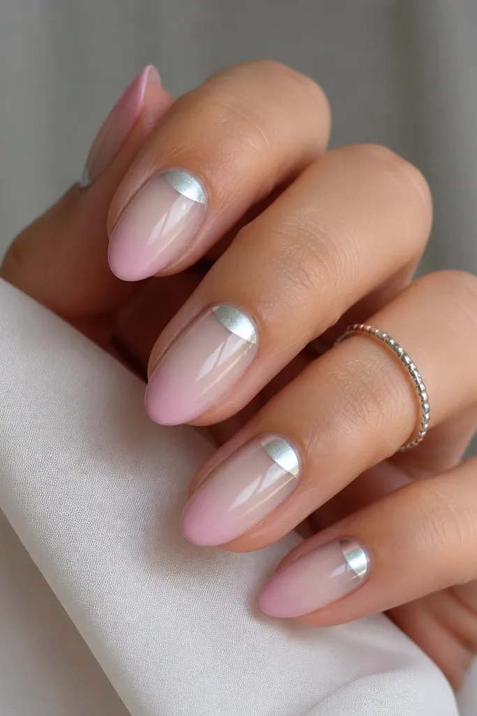 Short almond nails fading from sheer pearl nude at the base to pale pink at the tip. Silver chrome is mirror, with a soft moonlight glow centered in a crescent near the cuticle.