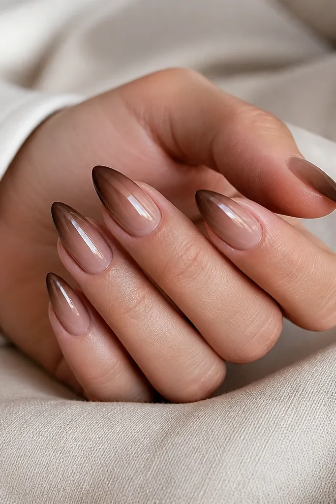 Short stiletto nails showing a smooth gradient from nude at the cuticle to chocolate brown at the tips. The ombre looks blended with no harsh line, and the nails are glossy.