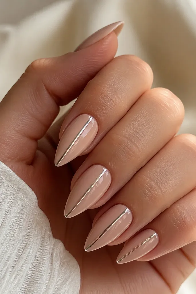 Short stiletto nails in soft nude. One thin chrome line runs straight down the center of each nail from near the cuticle to the tip, with a mirror-like shine.