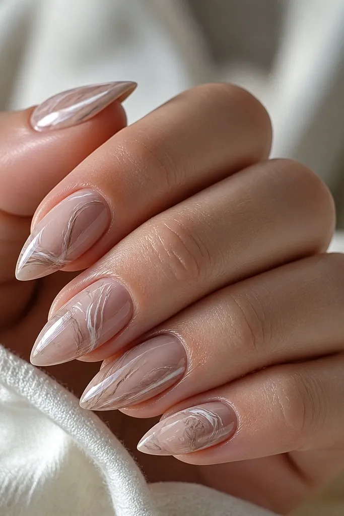 Short stiletto nails with a sheer nude base. Each nail has soft swirls of taupe and thin white lines, like marble, with a glossy finish.