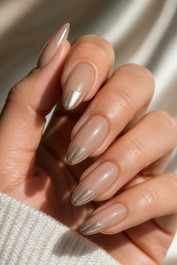 Natural nude beige ombre nails that fade into champagne gold chrome at the tips. The chrome is reflective and warm, showing gold highlights and soft mirror reflections.