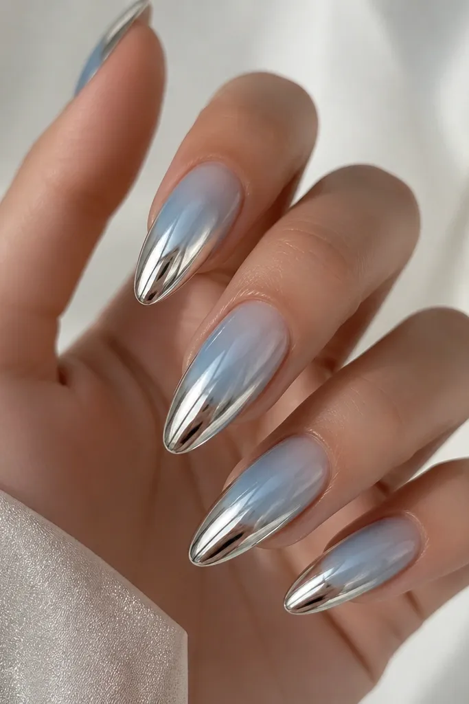 Almond nails with a translucent icy blue gradient that fades into bright silver chrome at the tips. The ombre looks like a cool wave, with a smooth transition and mirror-like chrome highlights.