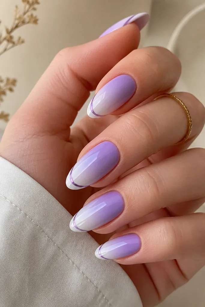 Removable ombre nails in a medium almond shape. Lavender fades toward a pale lilac near the tip, with a crisp chrome smile line just above the free edge in a lilac-violet tone.
