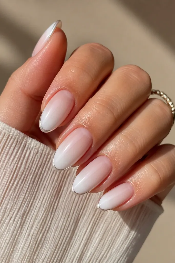Medium square nails with a white-to-clear ombre effect. A silver chrome French line follows a tight micro-curve at the free edge with a thin border, leaving the rest matte and soft.