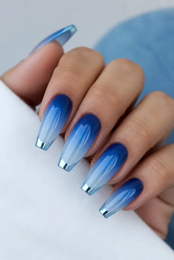 Medium coffin nails with a royal blue ombre that fades into a clear icy blue tip. Electric chrome forms a sharp cap on the very tip edge in a bright silver-blue tone.