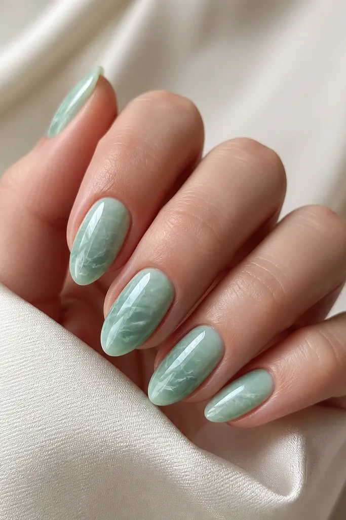 Short stiletto nails painted sea glass green, with irregular white marble veining across the surface. The marbling is thin and the nails are glossy.