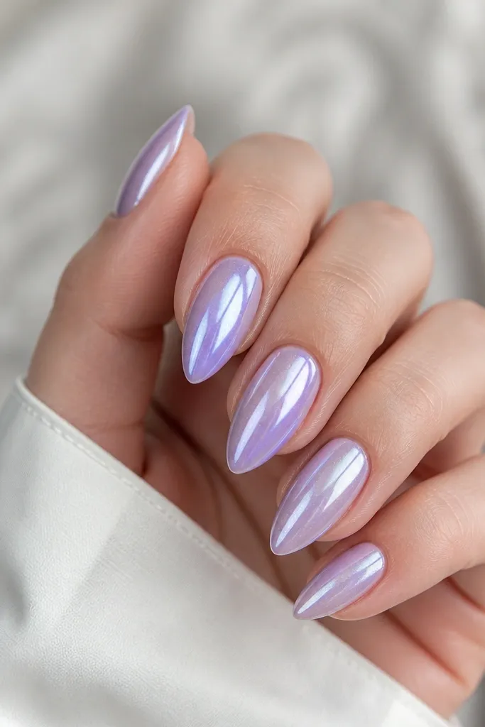 Short stiletto nails in a lavender base with a chrome dust effect that shifts from pale purple to silvery highlights. The nails are glossy underneath the chrome.