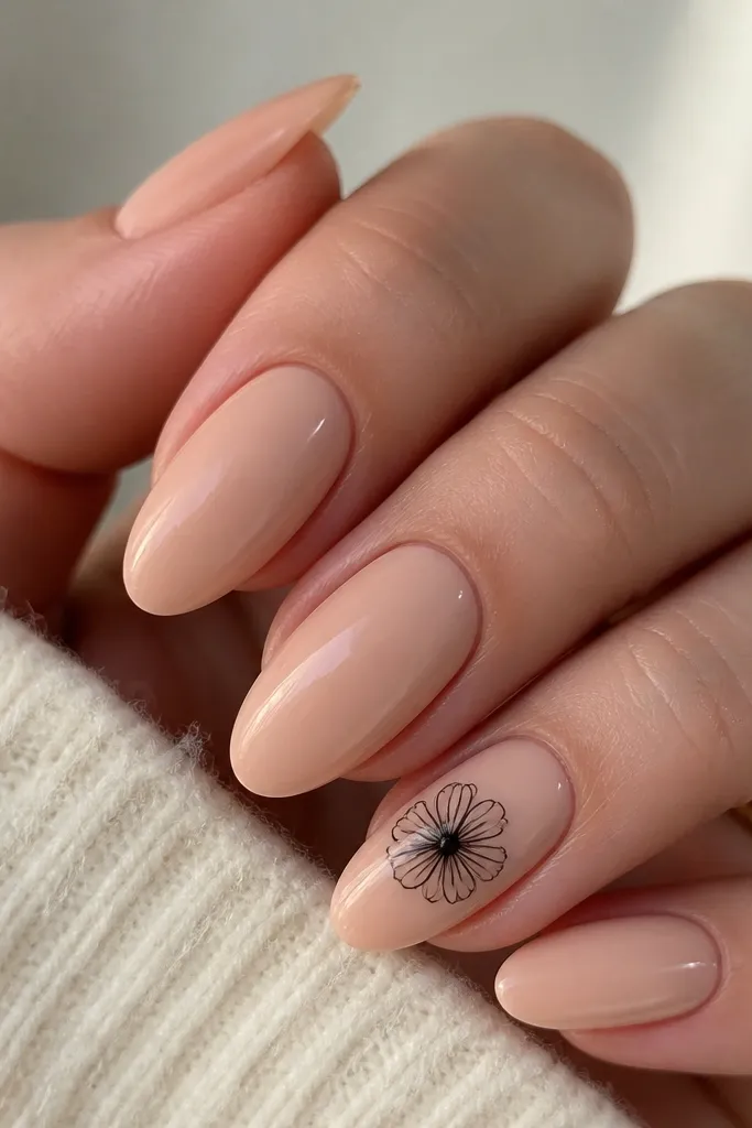 Cream nude nails. One accent nail per hand has a tiny black daisy with five petals and a small yellow dot center near the middle of the nail, glossy.