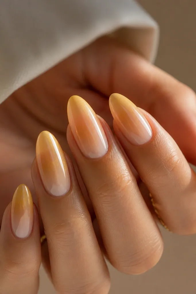 Almond nails with a warm ombré. The base is sheer nude at the cuticle, and the color fades into a soft golden amber near the tips.