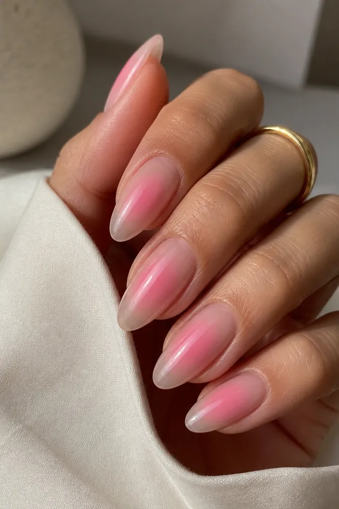 Longer almond nails painted with clear gloss on the base. A pink aura glow sits in the center of each nail, fading outward like a soft halo.