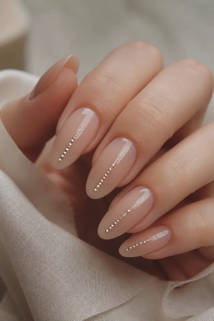 Nude almond nails with a glossy finish. A vertical line of small crystals runs from near the center down toward the tip, like a rain column.