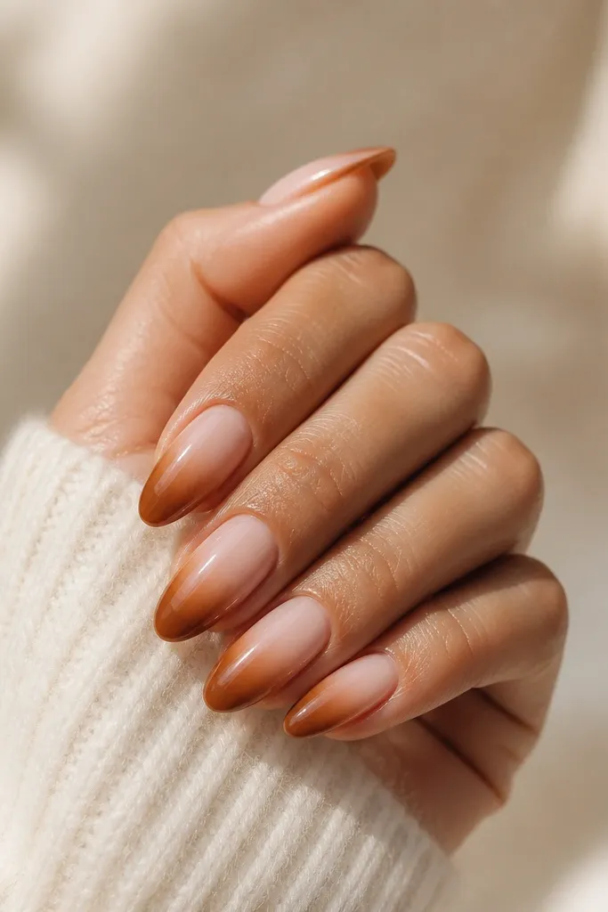 Short nails with a sheer nude base. The outer half of each nail fades into caramel brown toward the tip, like a soft ombré from the sides. The center stays lighter, and the finish is glossy.