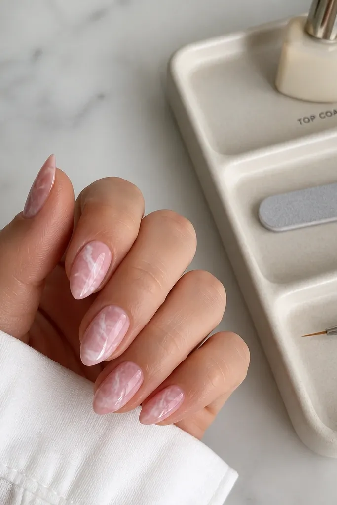 Short stiletto nails with pale pink and white marble veining, glossy. A small tray beside the nails shows labeled sections: "TOP COAT," "FILE," and "GEL LINER."