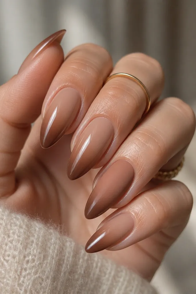 Short stiletto nails in caramel nude with a brown ombré fade toward the tips. Four nails are glossy; one accent nail is matte caramel with the same fade effect.