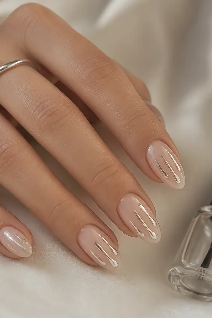 Short stiletto nails with nude glossy base. Each nail has a few silver gel "drips" starting near mid-nail and stopping before the tip edge. A mini top coat bottle sits on the side of the image.