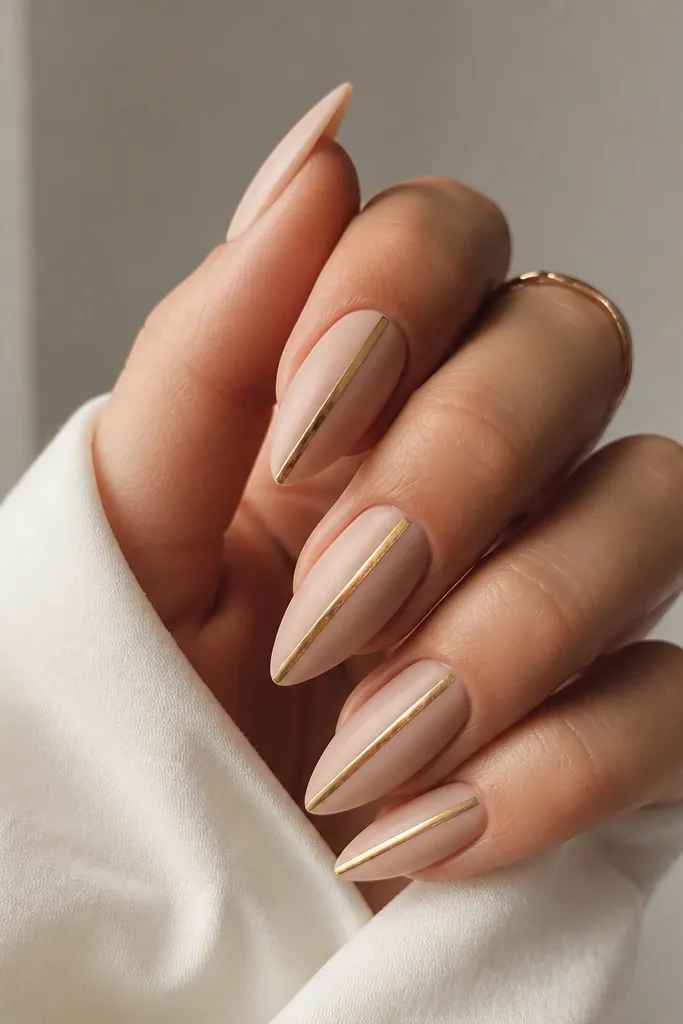Short stiletto nails in matte nude. One thin gold stripe runs straight down the center of each nail, crisp and reflective against the matte background.