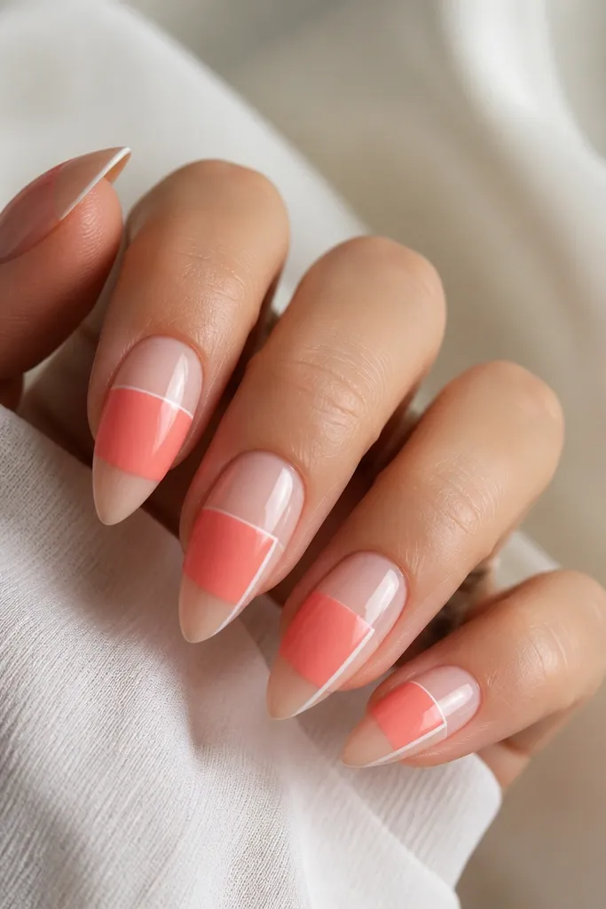 Short stiletto nails with glossy nude base. A coral block sits across the middle, separated by a thin white border line. Two nails show the border only on one side for variation.
