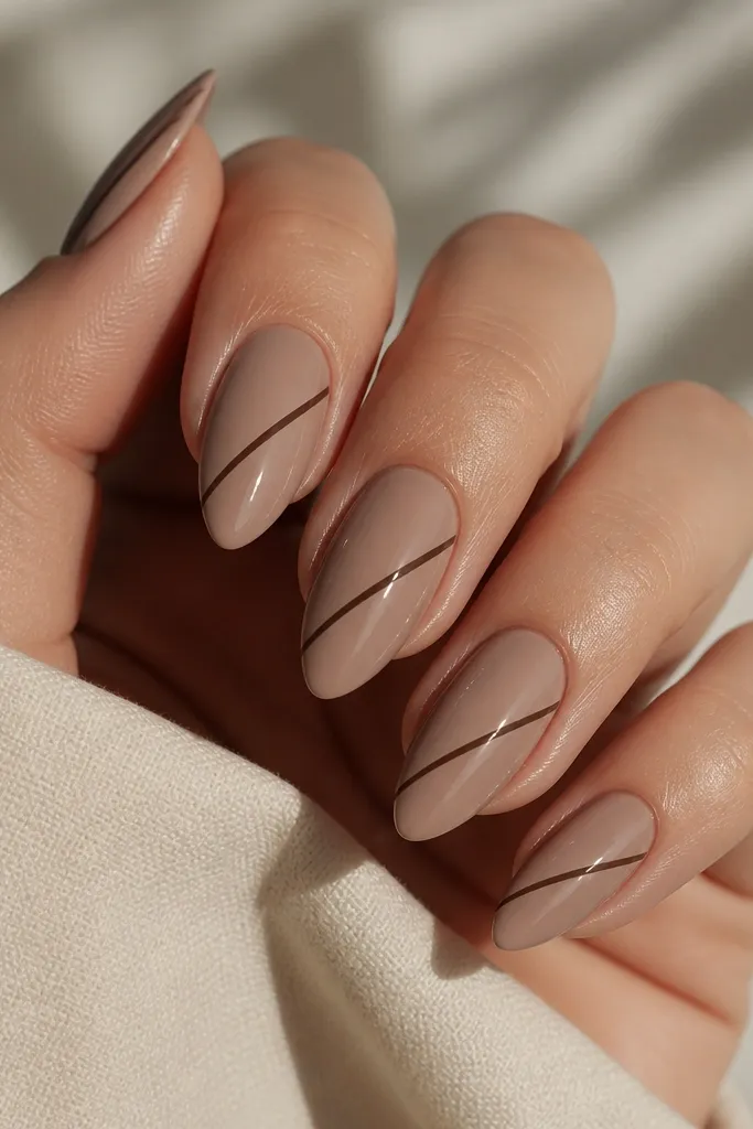 Short stiletto nails in mocha nude glossy. A thin dark brown diagonal stripe runs from lower left to upper right across each nail.