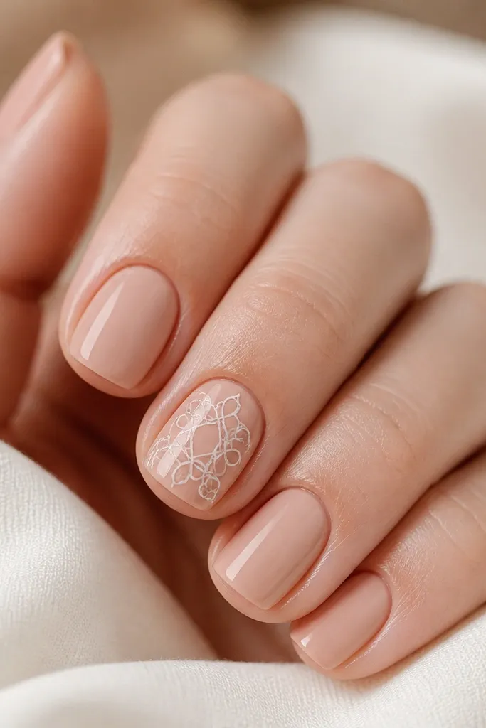 Four short nails in solid nude with glossy finish. One accent nail has a white lace-like outline pattern near the center, with connected loops, crisp and delicate.