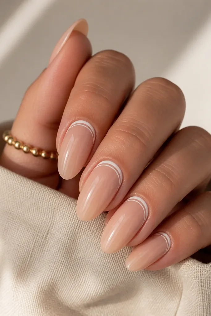 Short nails with nude base and two thin white lines forming a frame around the cuticle area. The lines are parallel and crisp, glossy finish.