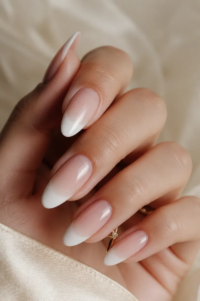 Short almond nails. Base fades from deeper nude at cuticle to lighter nude at mid nail, then a white French tip; glossy.