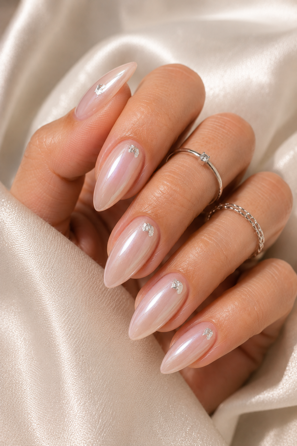 Short stiletto nails in icy pearly nude; one nail per hand has a small silver foil flake placed near the center of the nail; glossy top coat.