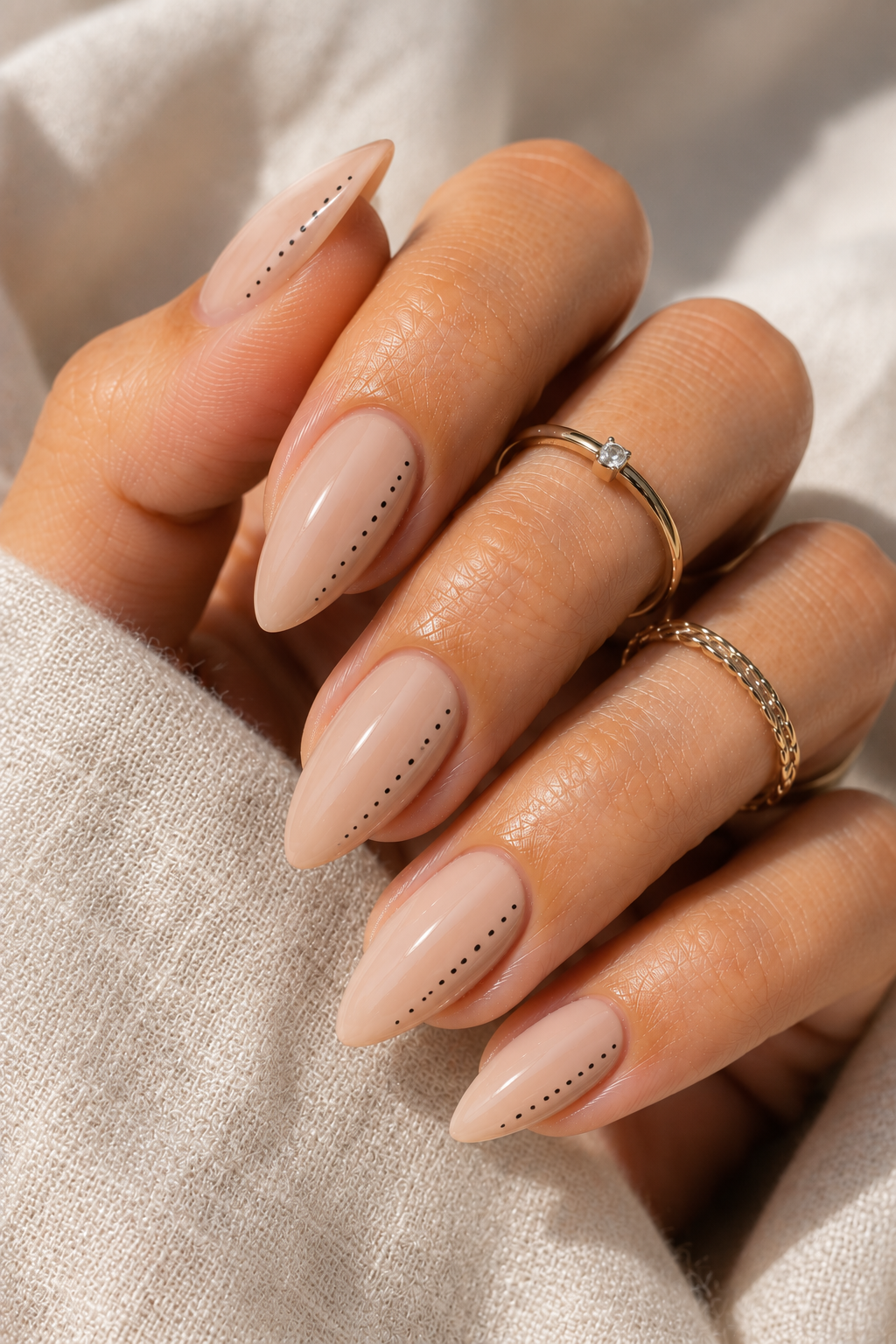 Short stiletto nails in nude pink; a line of tiny black dots runs down one sidewall from near the middle toward the tip; glossy finish.