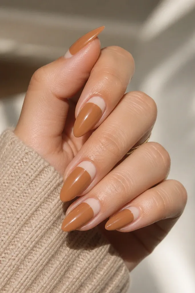 Short stiletto nails in warm caramel nude glossy; each nail has a glossy curved half-moon at the cuticle area in a slightly lighter nude; clean edges.