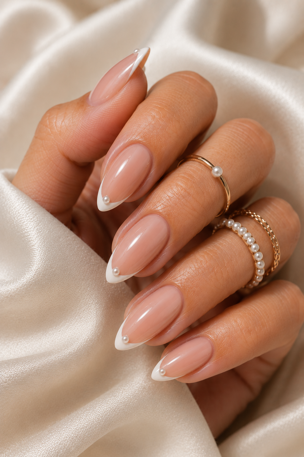 Short stiletto nails with nude base and a classic French tip; at the very center of each tip sits a tiny pearl bead, glossy and raised slightly; overall shiny finish.