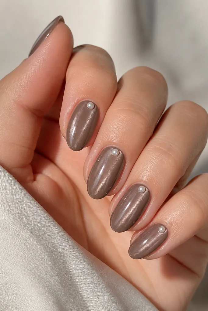 Short almond nails in taupe-brown cat eye. Each nail has one tiny pearl dot placed at the center cuticle area.