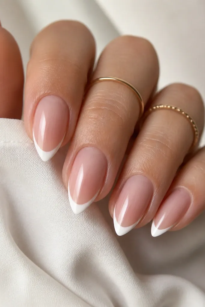 Five short stiletto nails with a sheer pink-blush base and a crisp, thin white French tip. The smile line is high and the corners taper to a sharp point.