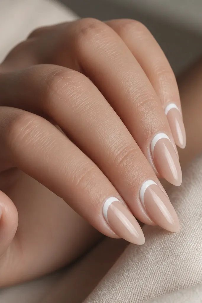 Short stiletto nails with a sheer nude base. The white is painted along the inner cuticle curve, and the outer edge is left natural.