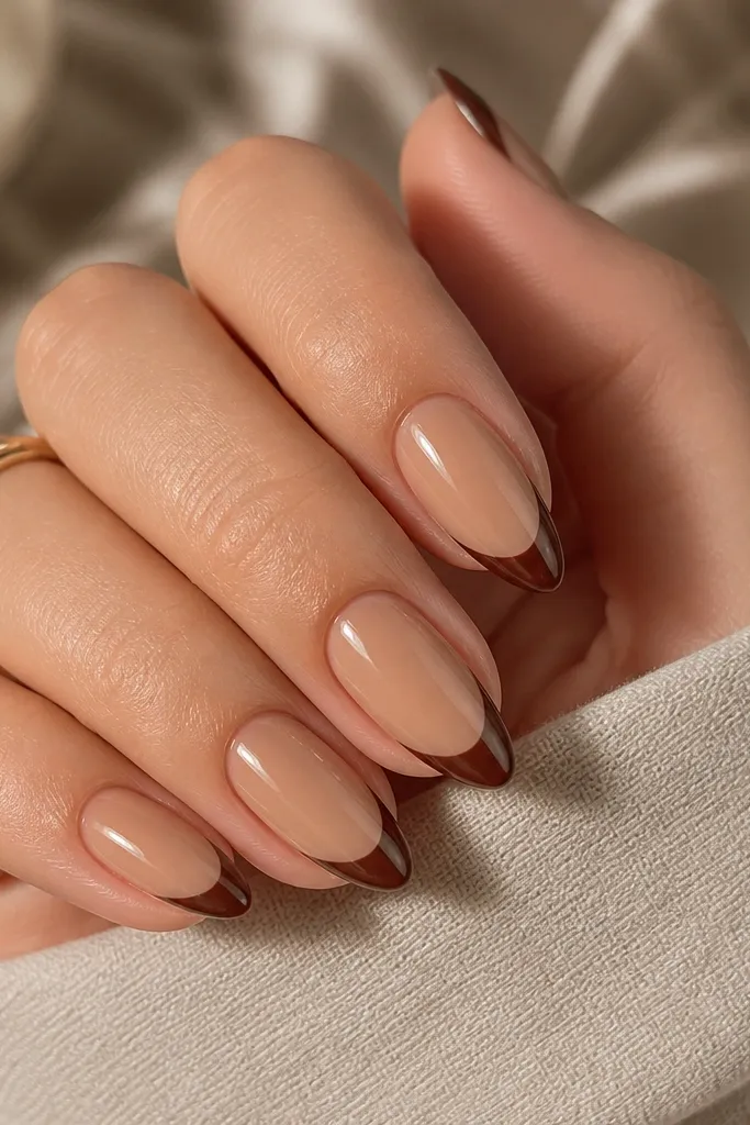 Short stiletto nails with a caramel nude base. The french tips are chocolate brown with a crisp smile curve and tapered point. The finish is glossy and smooth.