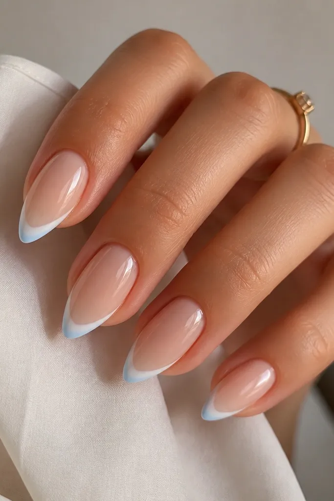 Short stiletto nails with milky nude base. The french tips are mostly white, but the outermost edge near the point has a faint soft blue tint. The blue fades inward, creating a cool accent.