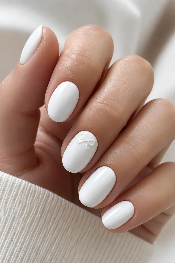 Short oval nails fully opaque white and glossy. One accent nail has a tiny white bow with thin shadow lines, placed near the cuticle; other nails stay plain.